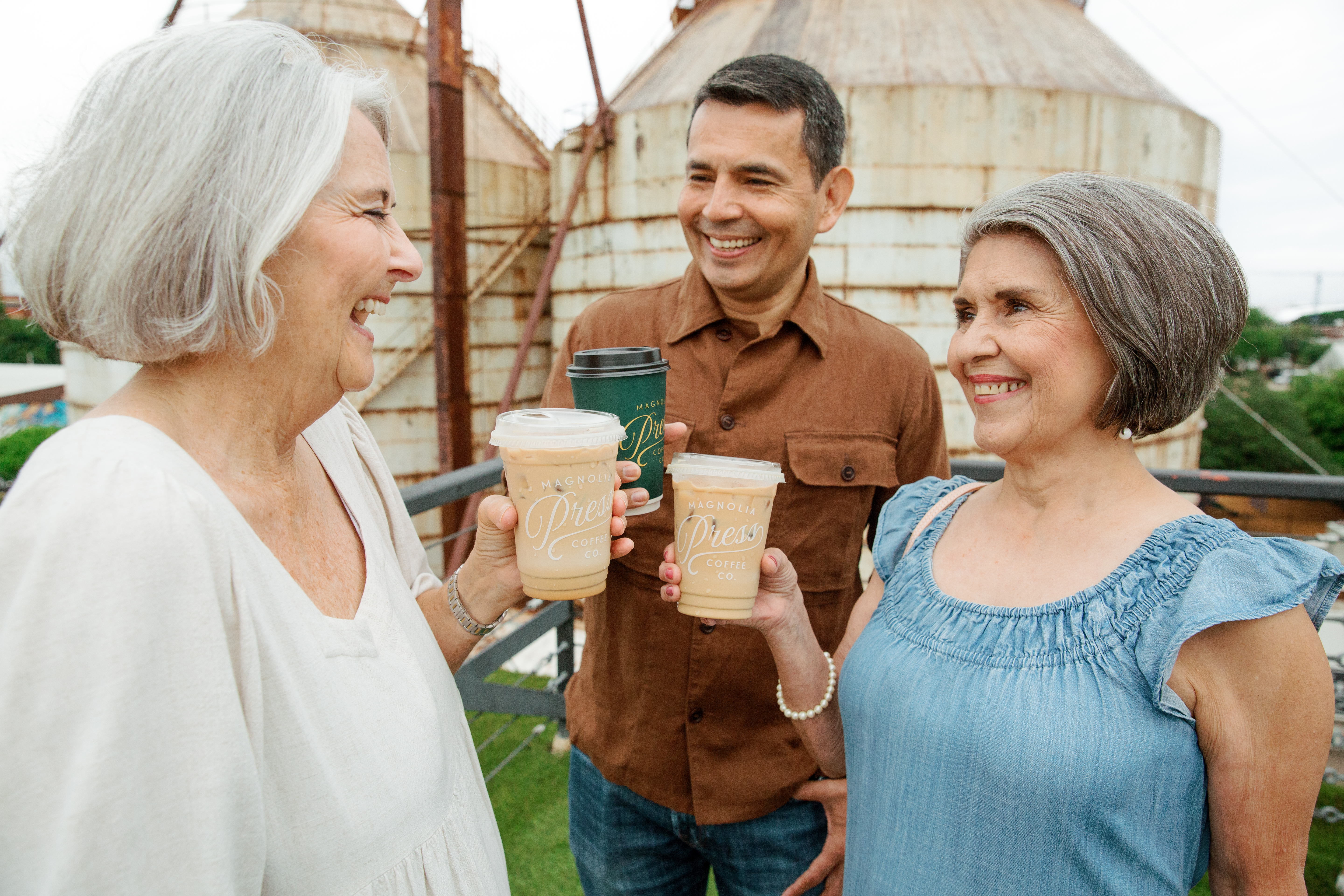 3 people chatting and smiling atop the roof at the Magnolia Market. They are all holding drinks from Magnolia Press.