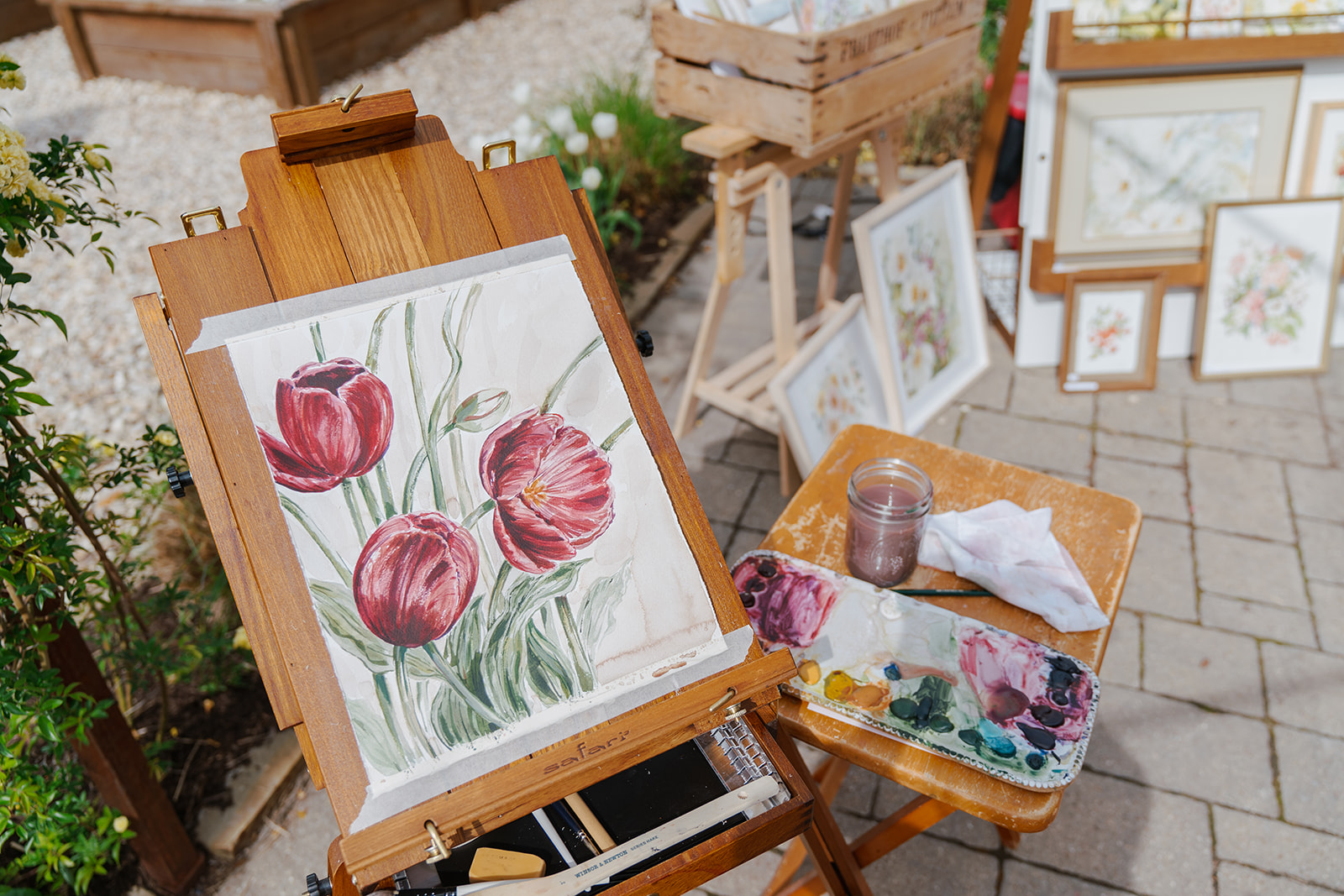 A painting of pink tulips on a canvas held up by an easel. Several other paintings are scattered around.