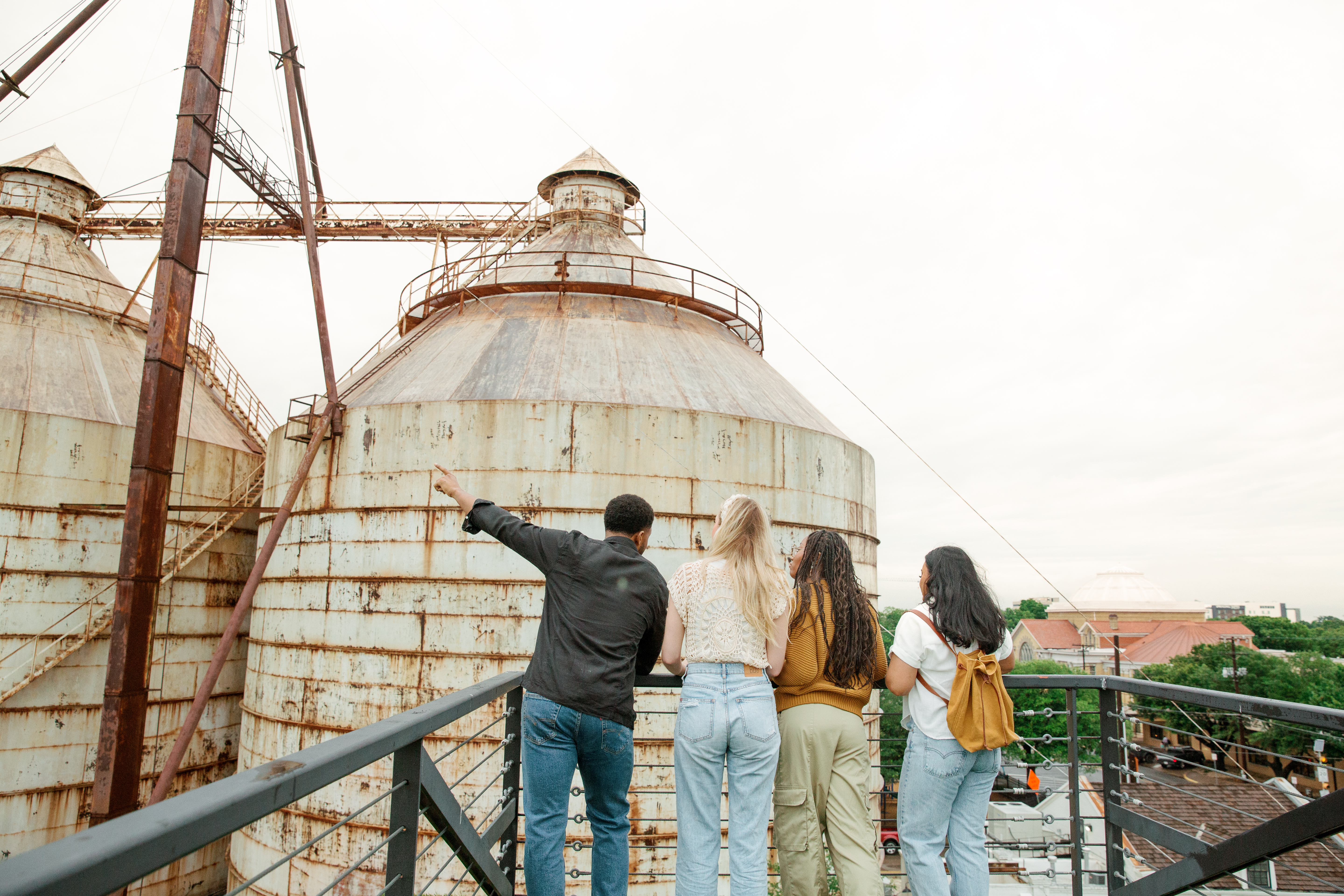 4 people standing atop the roof at the Magnolia Market. One is pointing towards the Silos.