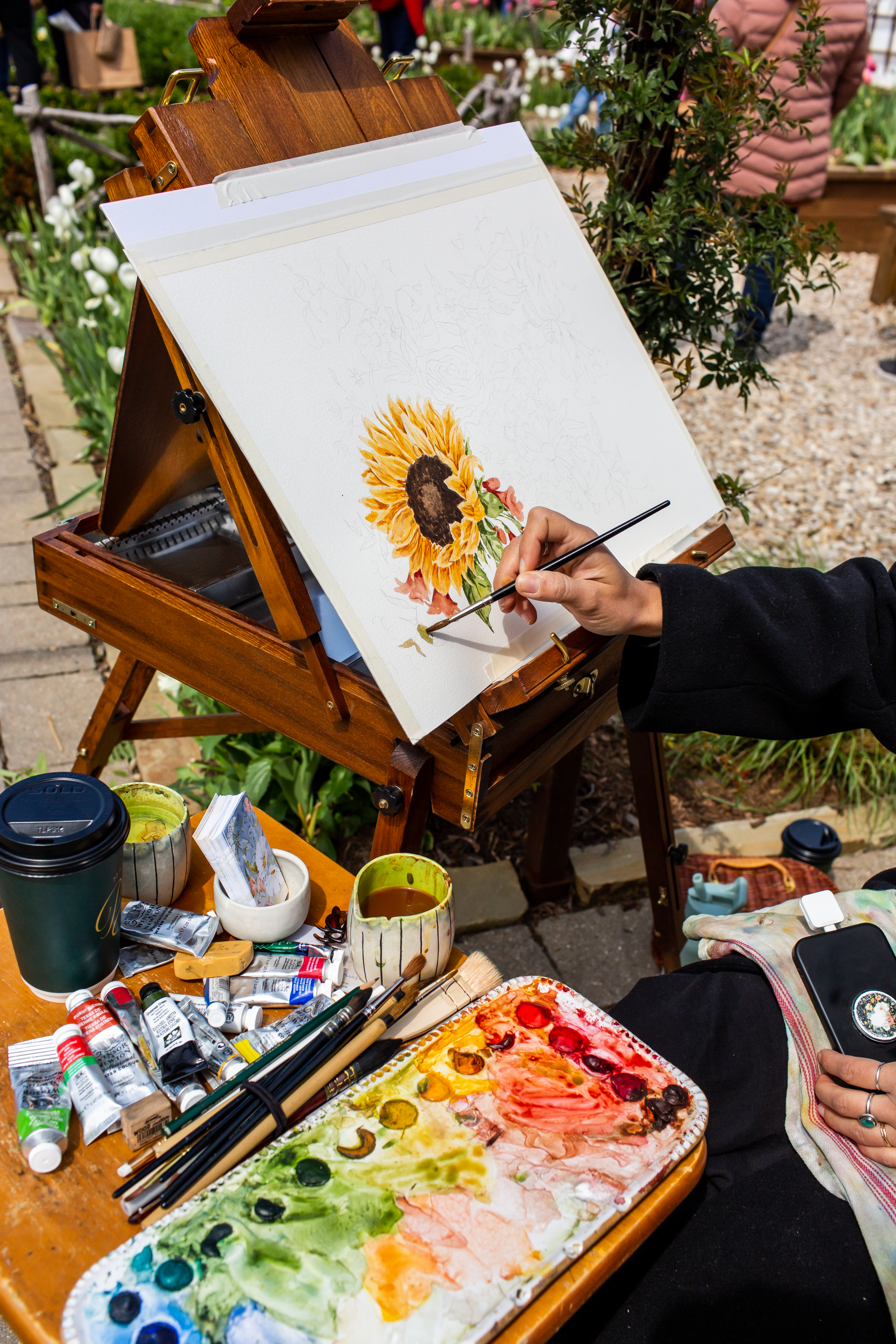 A person painting a sunflower on a canvas held up by an easel.