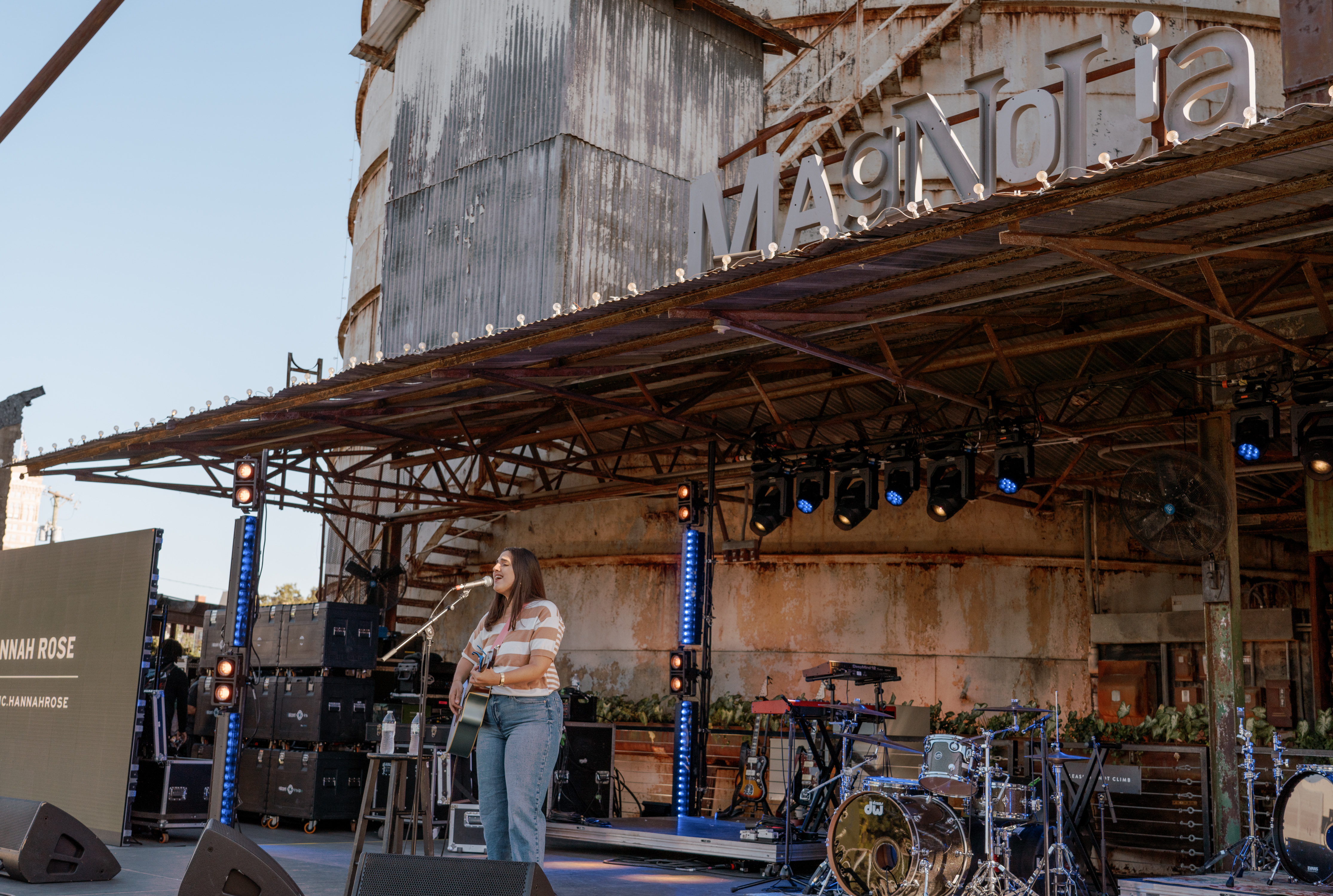 A musical artist singing and playing the guitar on the Magnolia Lawn live stage.