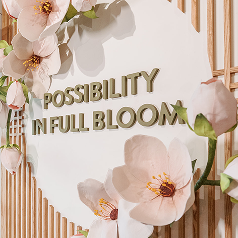 A white wall reads "possibility in full bloom" surrounded by wooden slats and light pink flowers. 