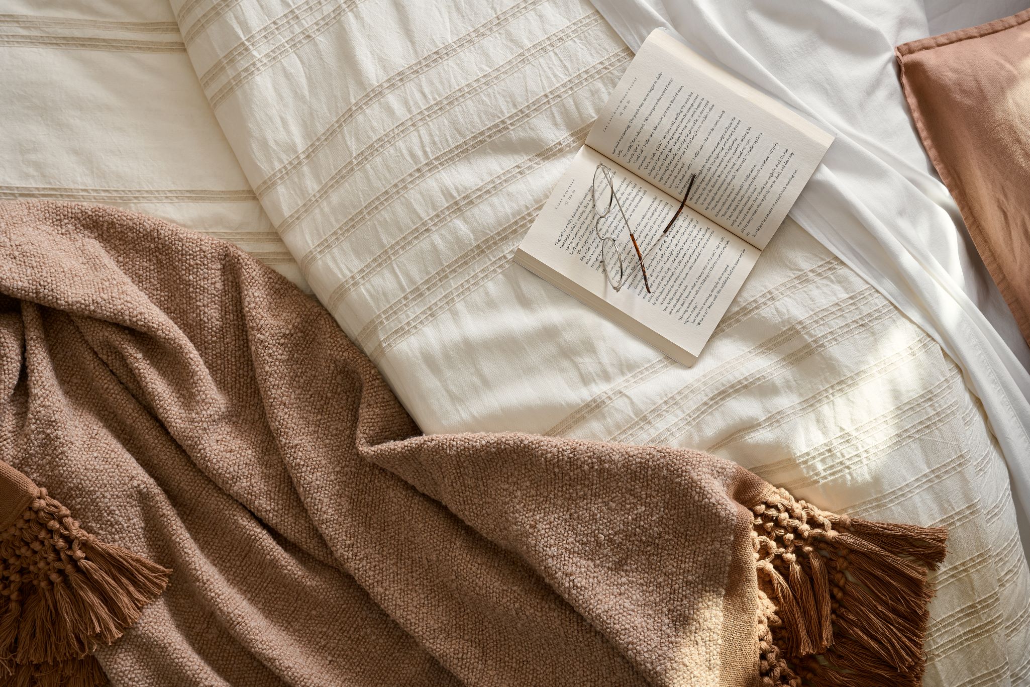a bed with a white duvet and rust colored throw blanket and an open book