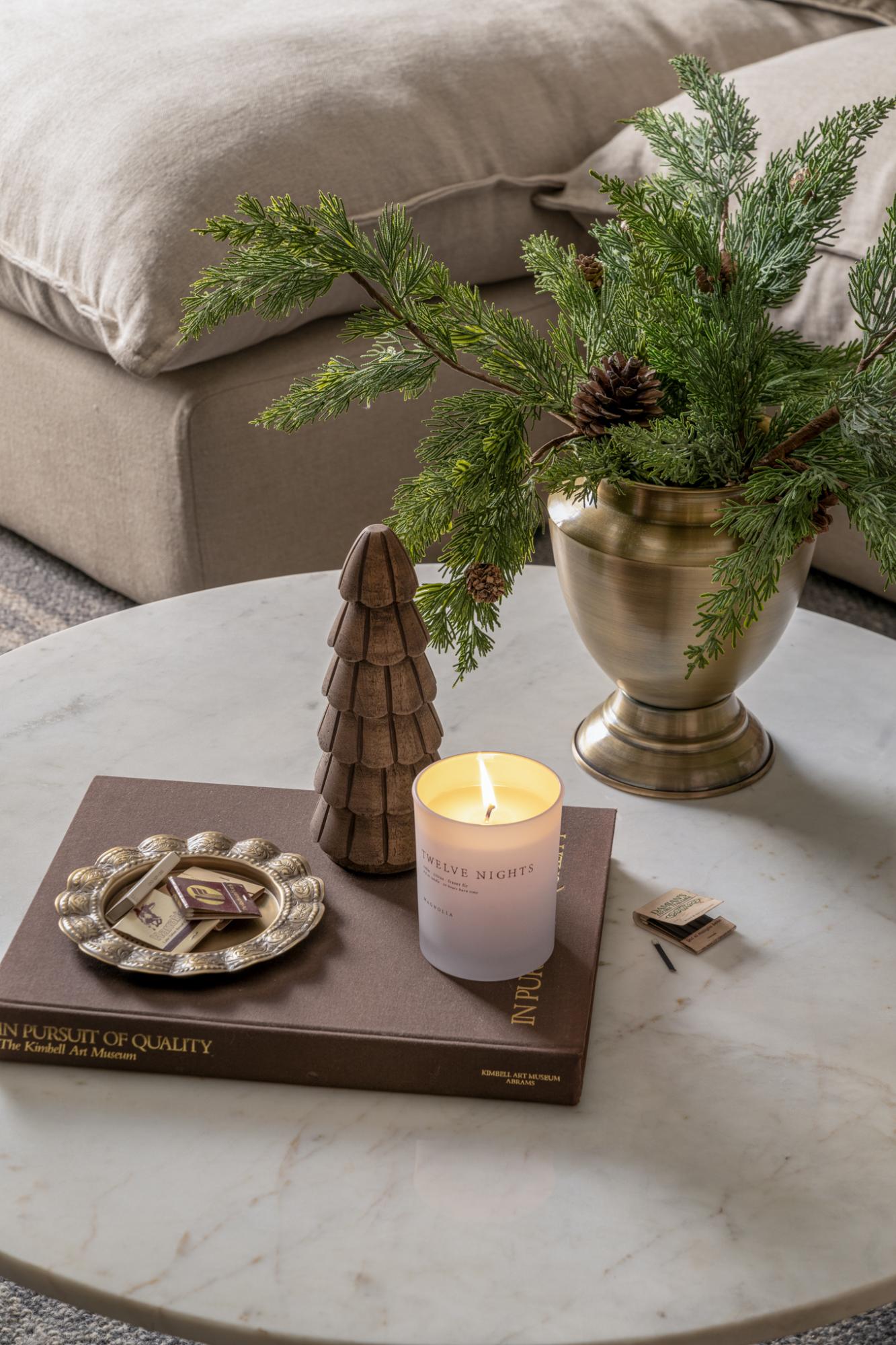 A white coffee table is filled with holiday decor—like a wooden tree, metal tray, festive candle, and more.