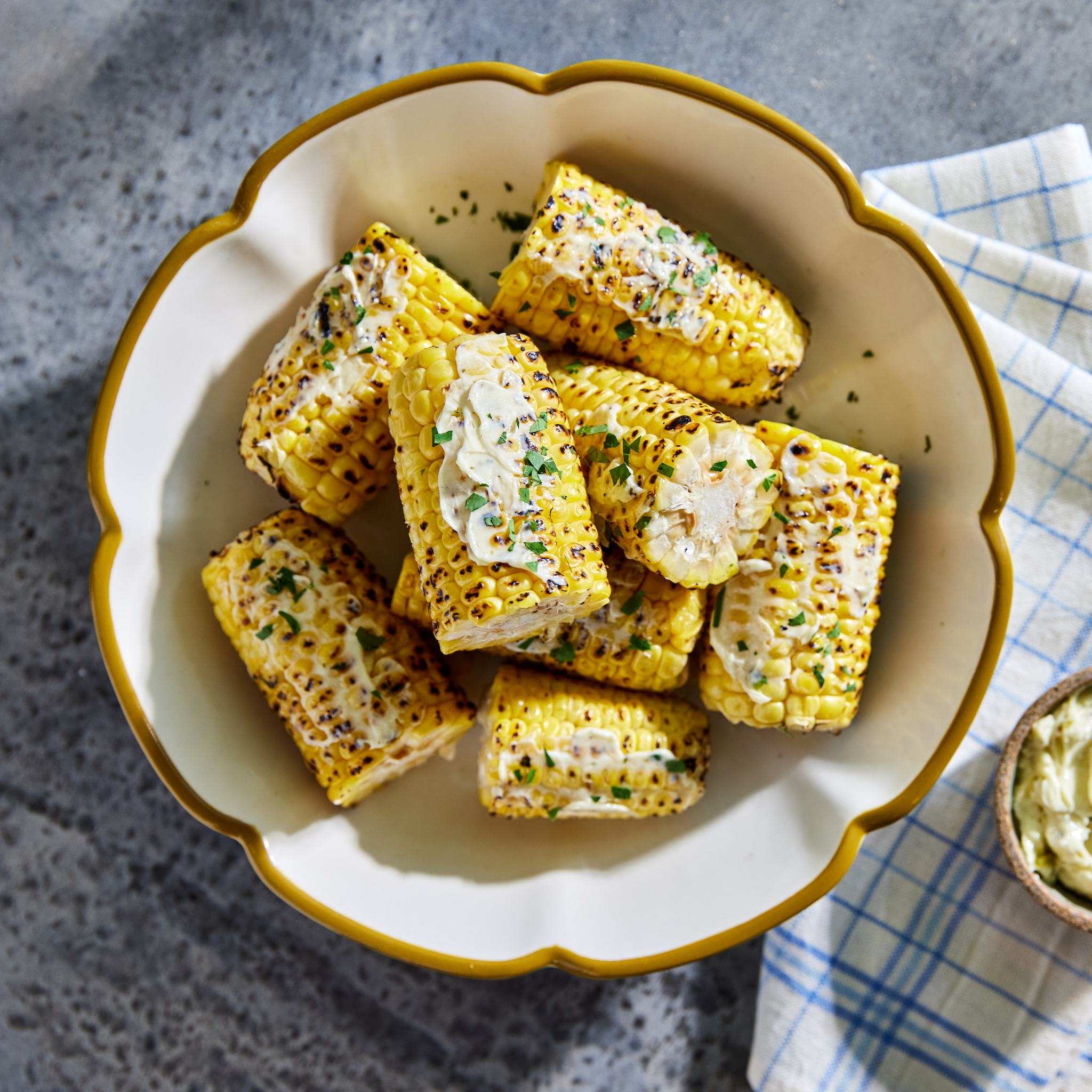 Corn on the cob is topped with butter in a white bowl with a yellow rim.