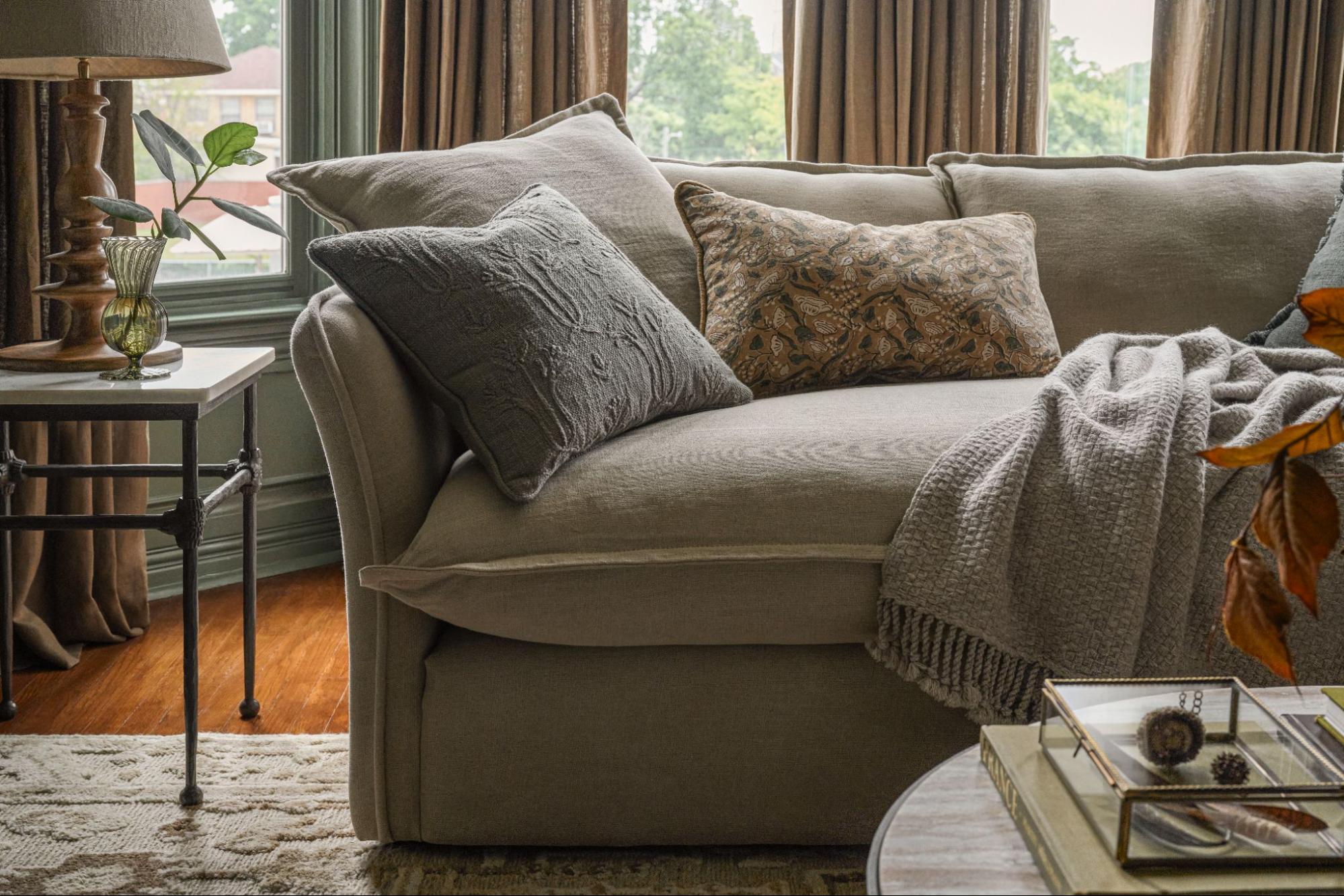 Plush neutral couch with throw pillows, blanket, and side table