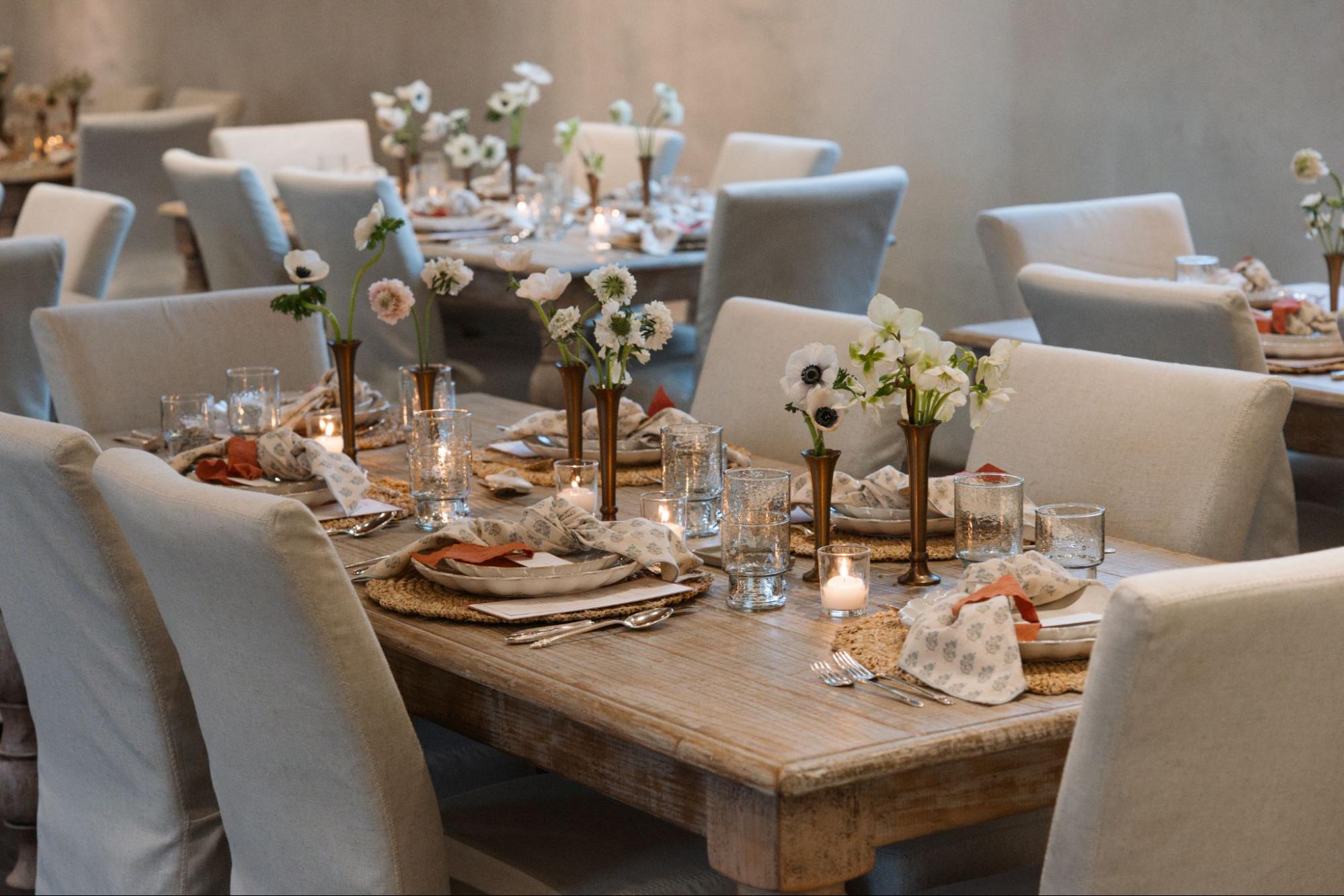 A wooden table from Magnolia is topped with a spring-inspired tablescape, including block-printed napkins, brass bud vases, scalloped dishes, and more. 