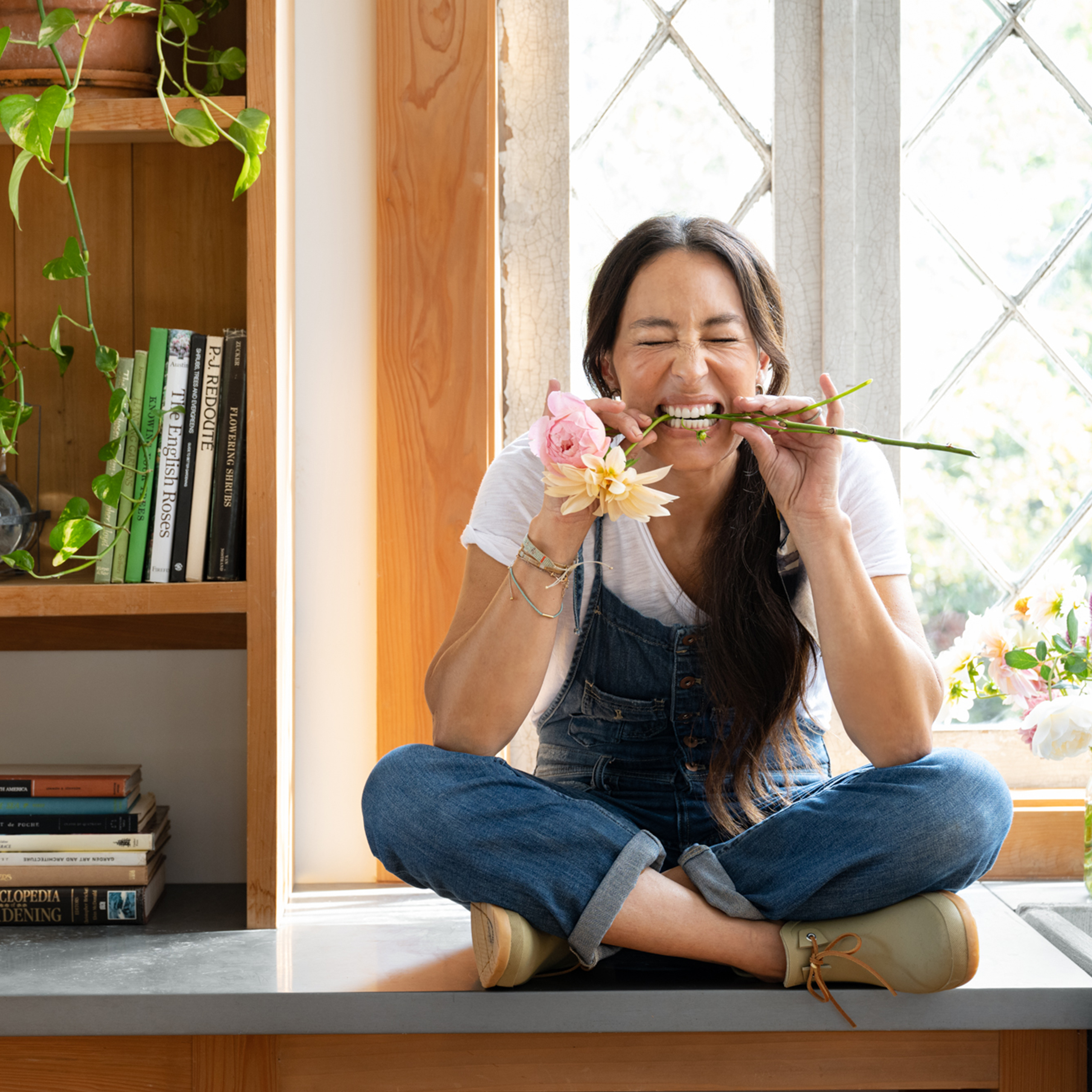 Joanna Gaines sitting on the counter in her garden shed with dahilia stems in her mouth