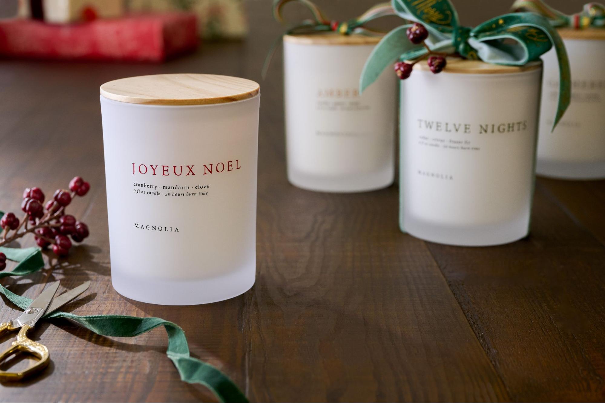 Three Magnolia candles are surrounded by green ribbon and red berries.