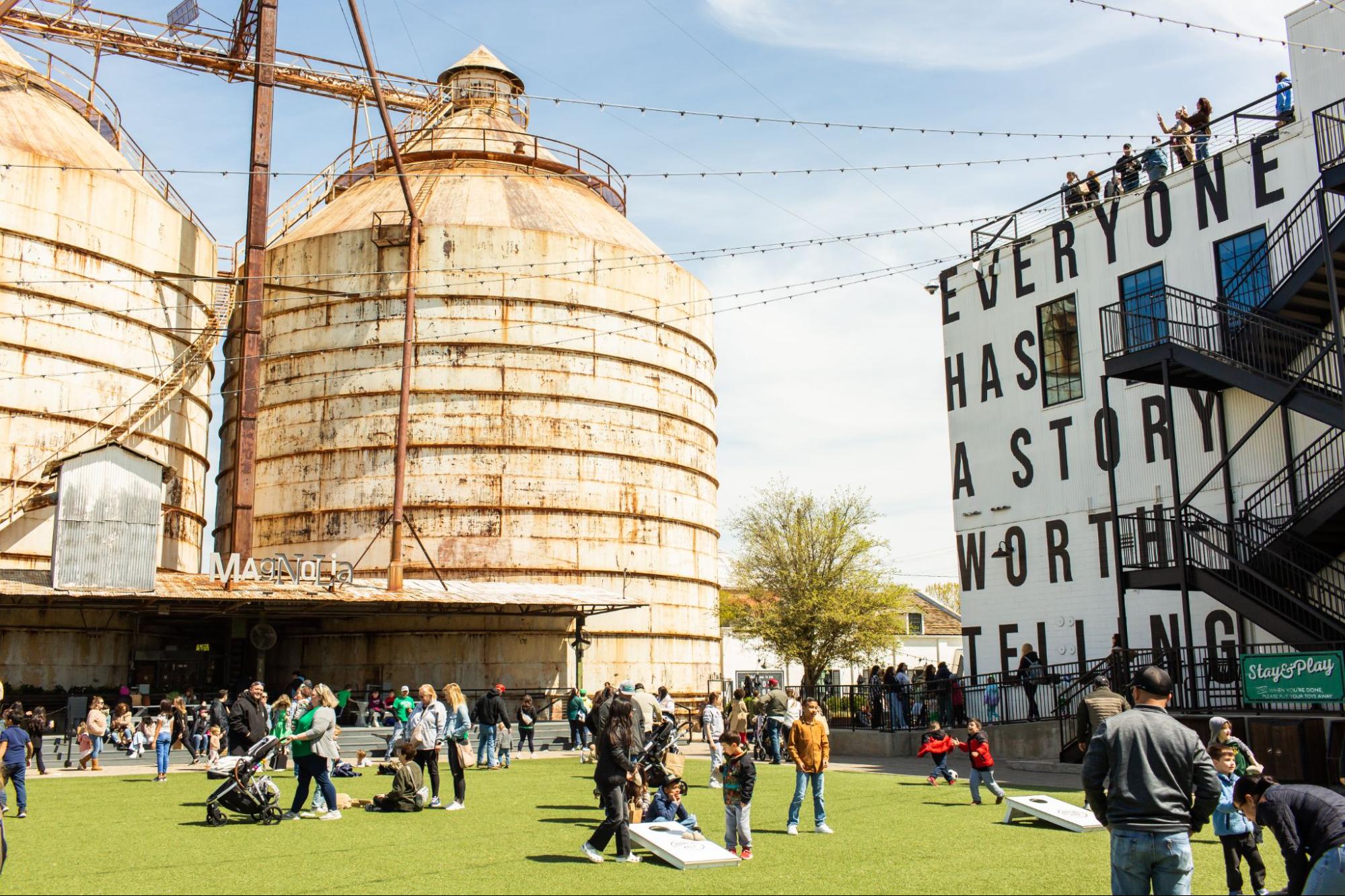 The Magnolia Silos stand in front of a green lawn surrounded by people in Waco, Texas.